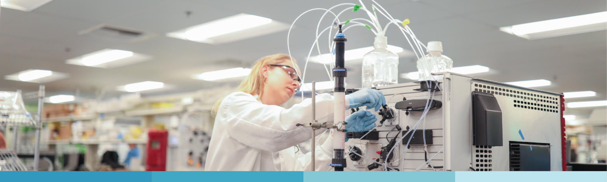 Female scientist wearing safety goggles adjusting laboratory equipment with tubing