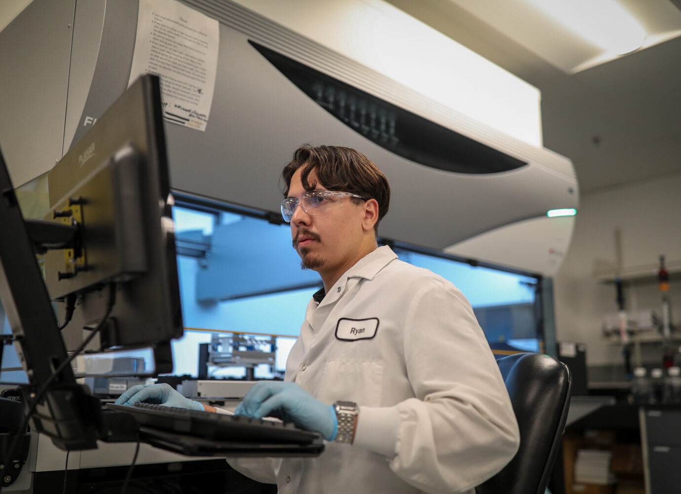Male employee wearing safety glasses working at a computer workstation in a facility