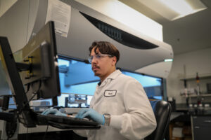 Male employee wearing safety glasses working at a computer workstation in a facility