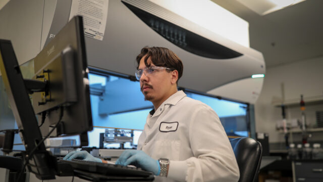 Male employee wearing safety glasses working at a computer workstation in a facility
