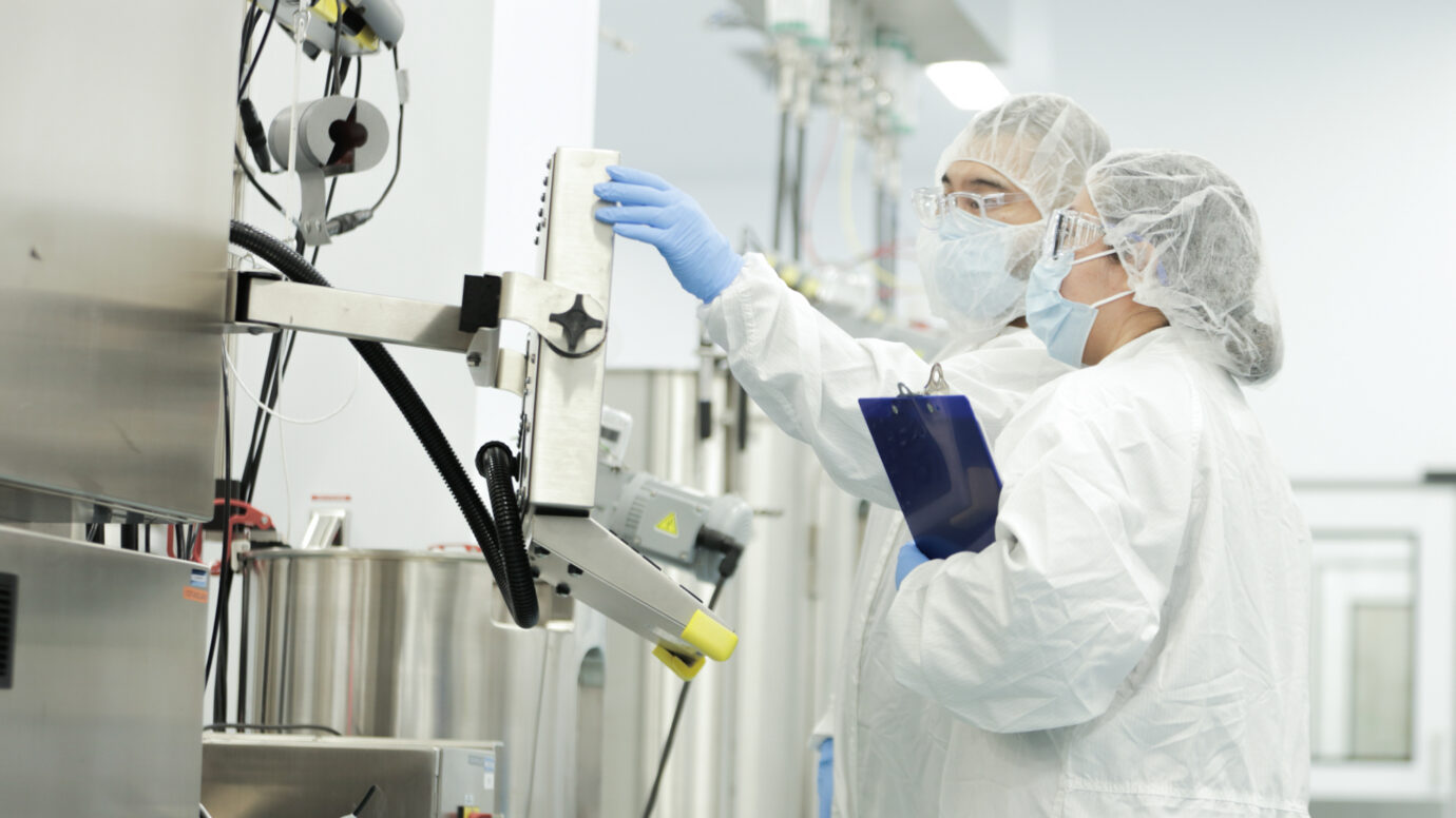 Two cleanroom technicians in full PPE operating manufacturing equipment