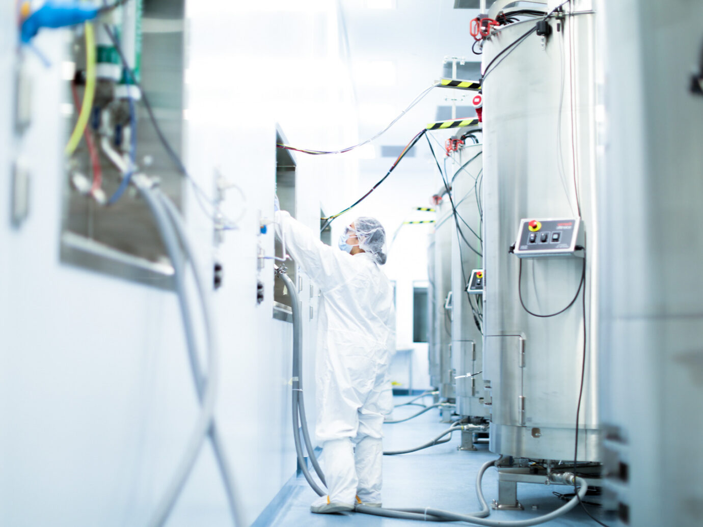 Technician in cleanroom PPE operating large bioreactor manufacturing equipment