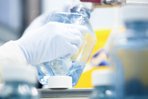 Gloved hand holding a bottle of orange liquid in a manufacturing cleanroom