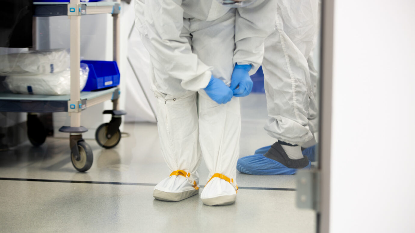 Technician in a cleanroom suit pushing a cart in a manufacturing facility