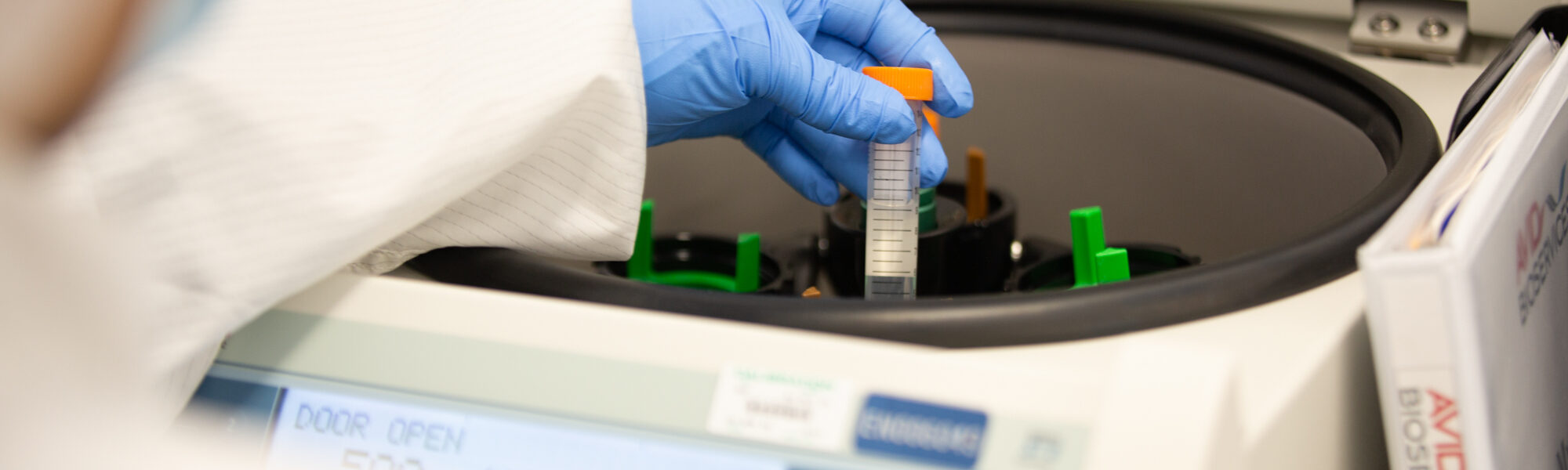 Gloved hand placing a sample tube into a centrifuge