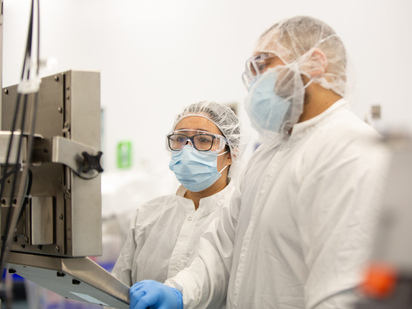 Two cleanroom technicians in hairnets and masks operating equipment