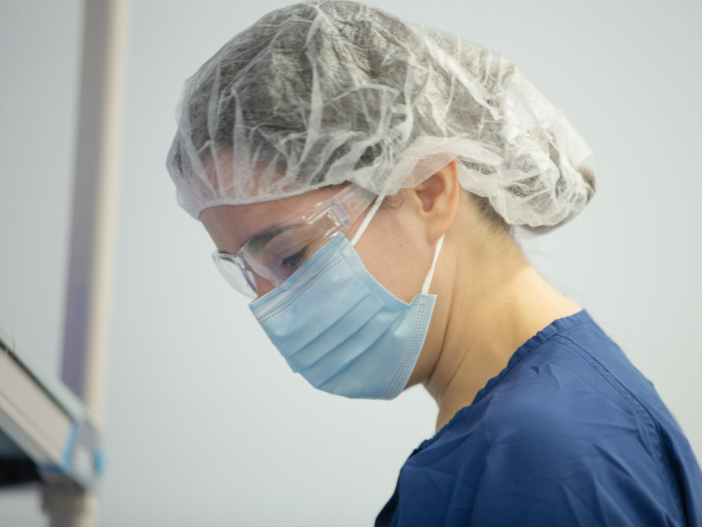 Cleanroom worker wearing a hairnet and mask looking down