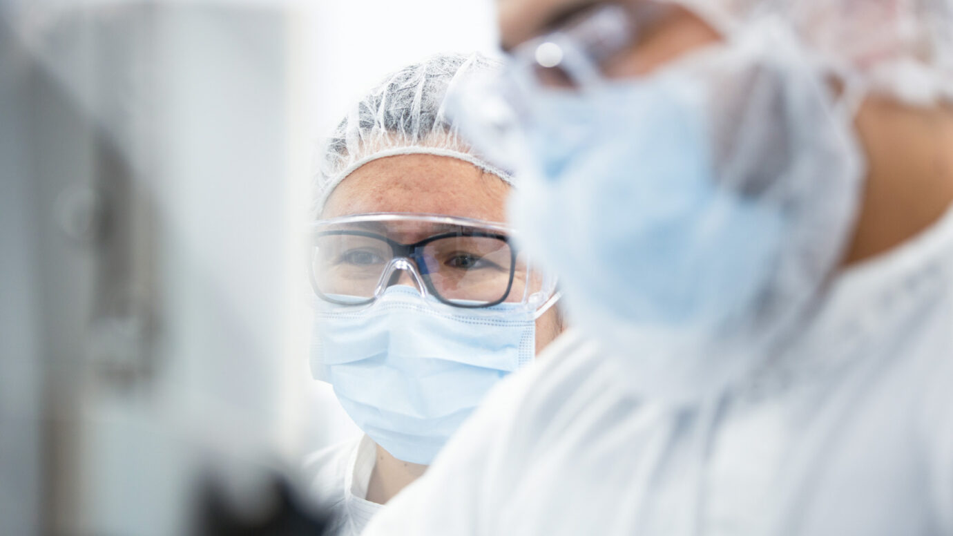 Close-up of a technician wearing a hairnet, safety glasses, and mask in a cleanroom