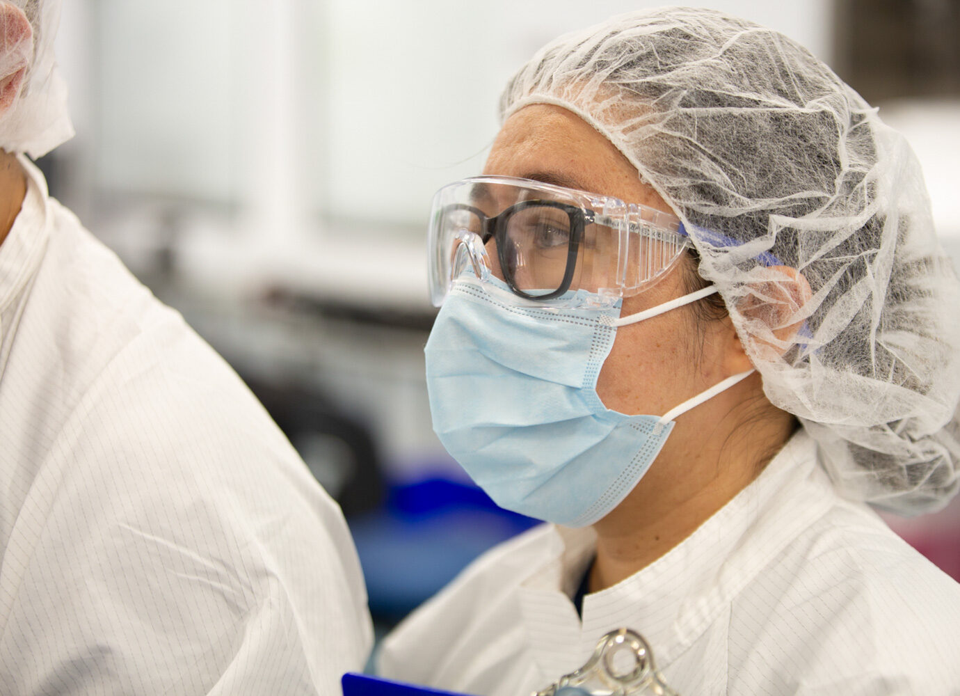 Close-up of a worker wearing safety glasses, a face mask, and a hairnet in a cleanroom