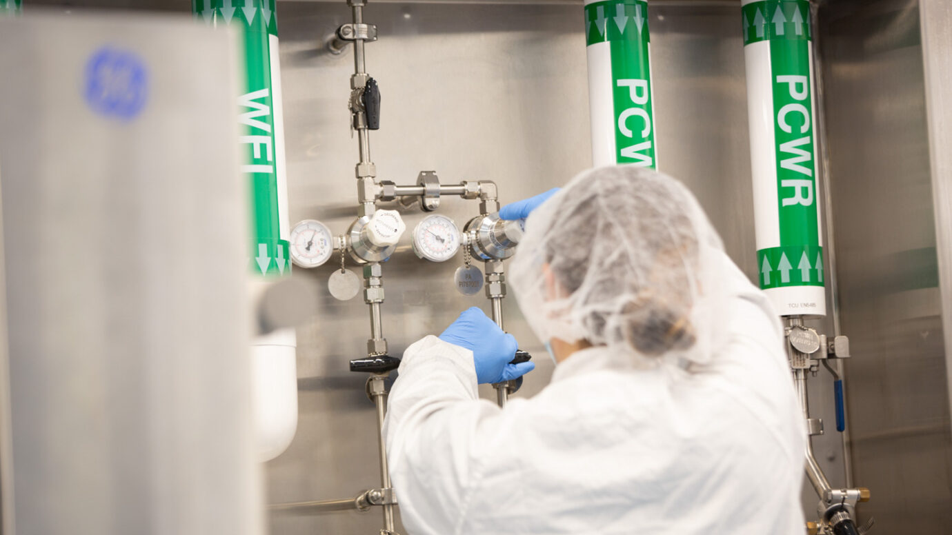 Technician in a hairnet adjusting valves on labeled gas supply lines in a manufacturing suite