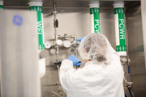 Technician in a hairnet adjusting valves on labeled gas supply lines in a manufacturing suite