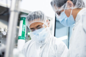 Two cleanroom workers in masks and hairnets standing beside vials on a rack