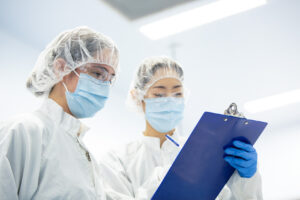Two cleanroom technicians in hairnets and masks reviewing documentation