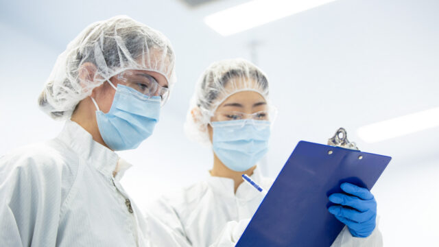 Two cleanroom technicians in hairnets and masks reviewing documentation