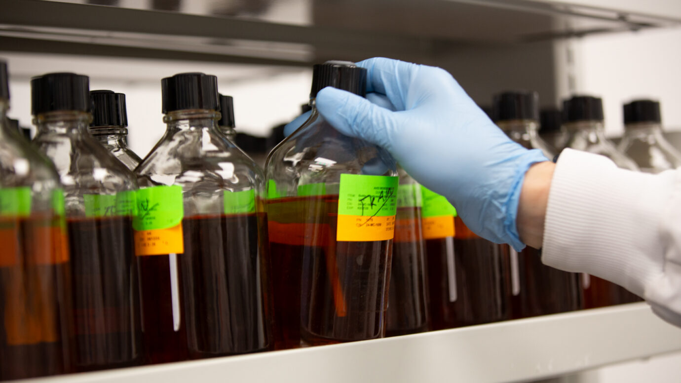 Gloved hand selecting a labeled reagent bottle from a shelf
