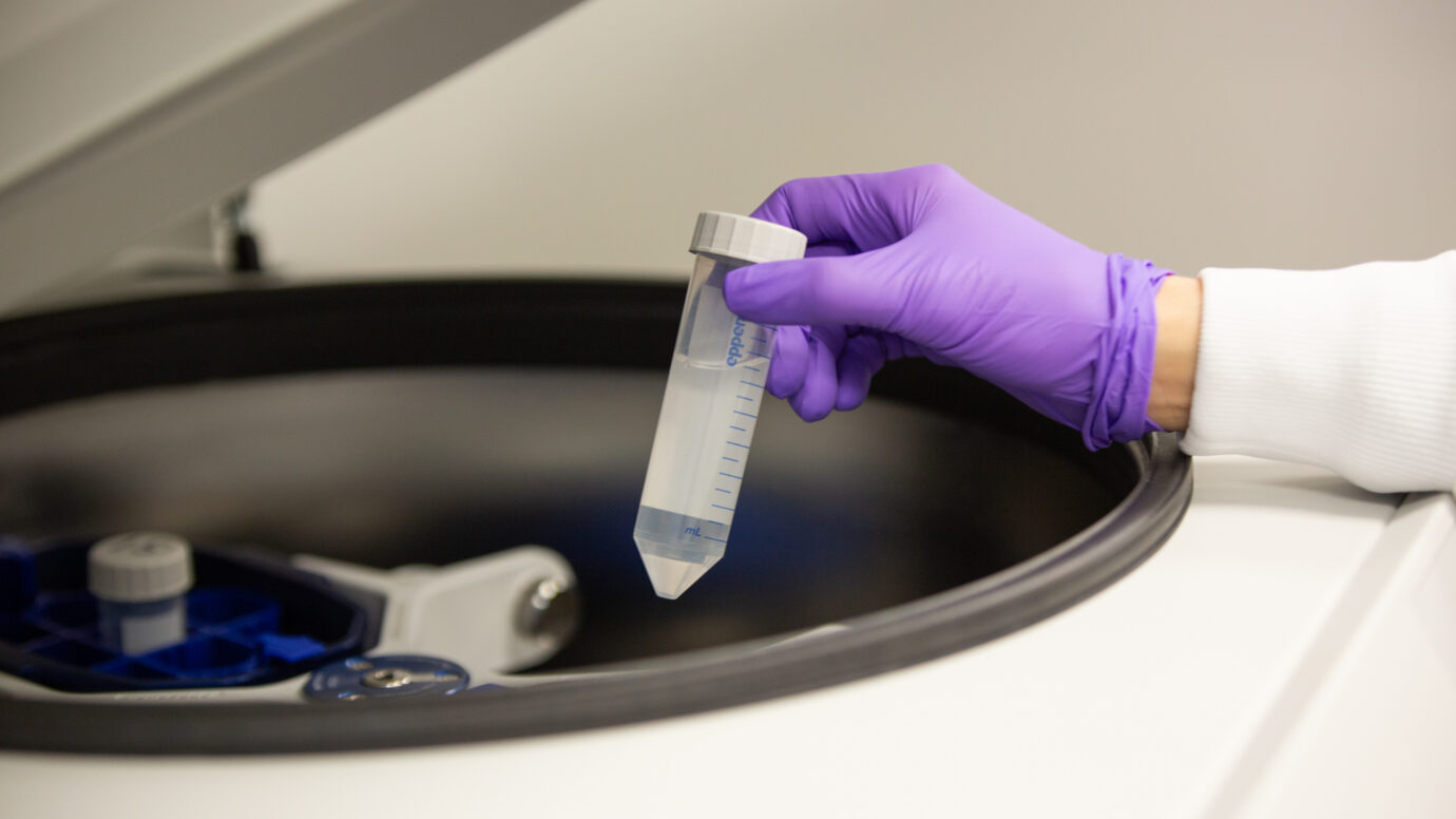 Purple-gloved hand holding a graduated laboratory container