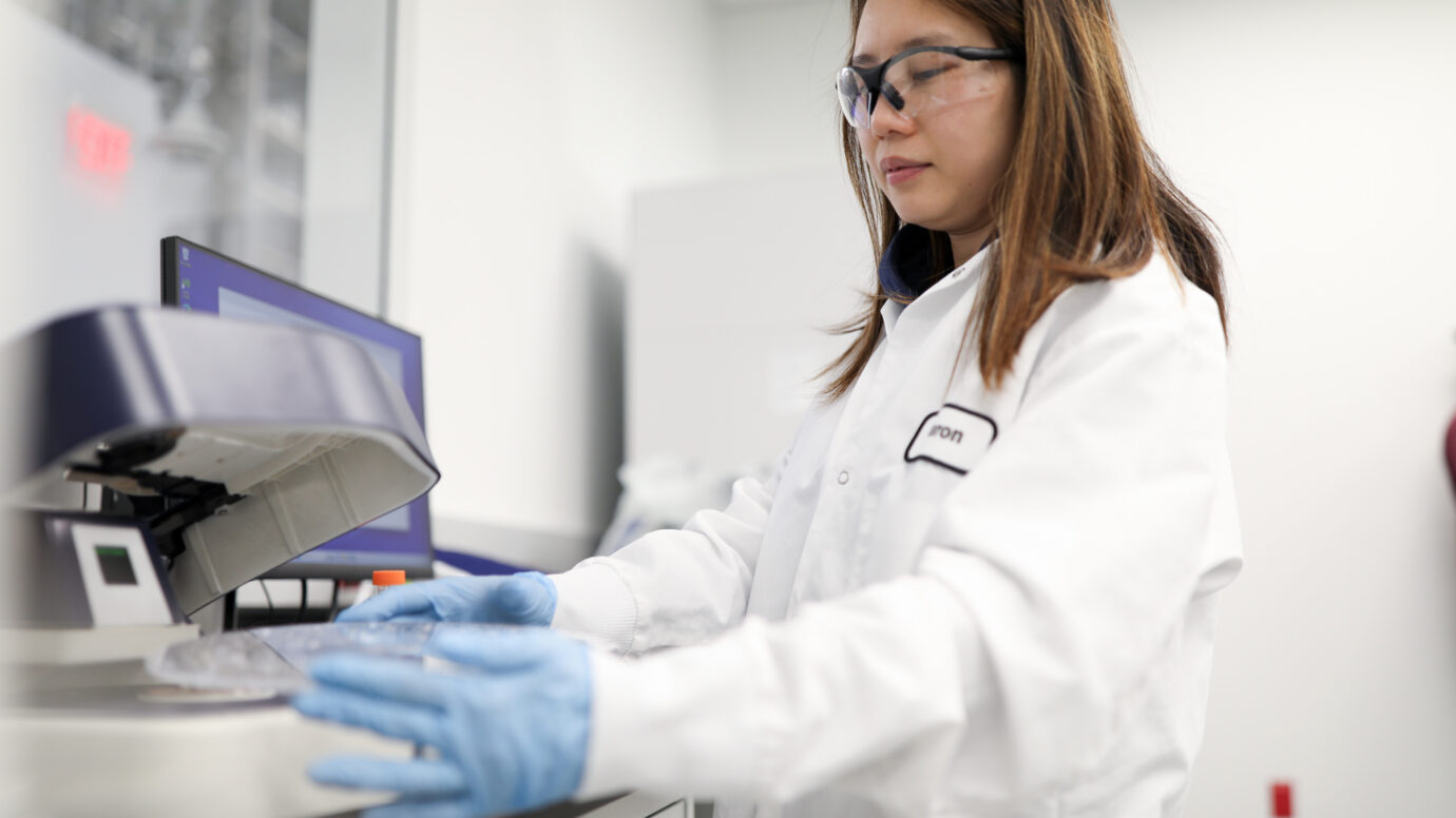 Female lab worker wearing safety glasses next to laboratory equipment