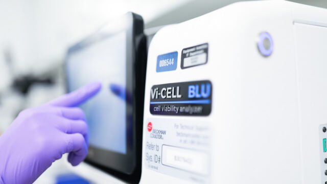 Gloved hand operating a Vi-CELL BLU cell viability analyzer