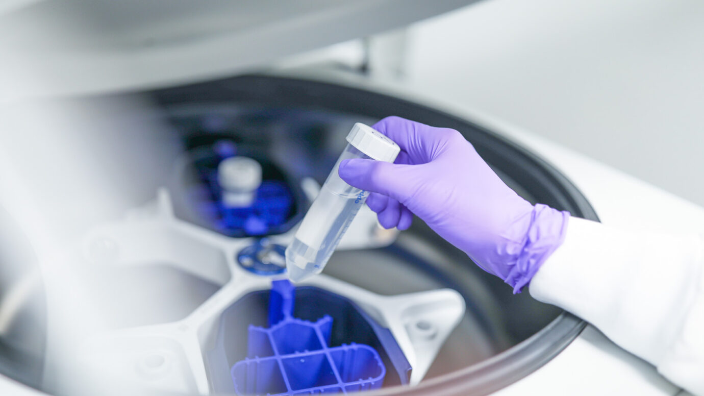 Gloved hand holding a small sample vial in a cleanroom