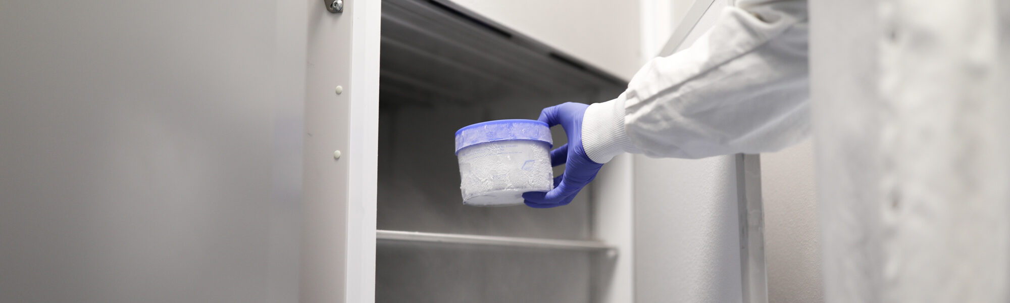 Gloved hand in a cleanroom placing a sample container into a biosafety cabinet
