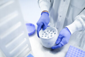 Gloved hands holding a multi-well sample tray in a lab