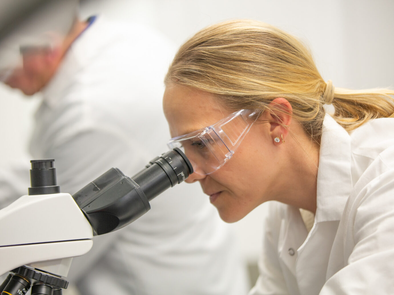 Female scientist wearing safety glasses looking through a microscope in a lab