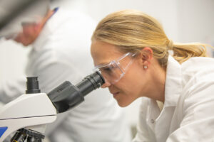 Female scientist wearing safety glasses looking through a microscope in a lab