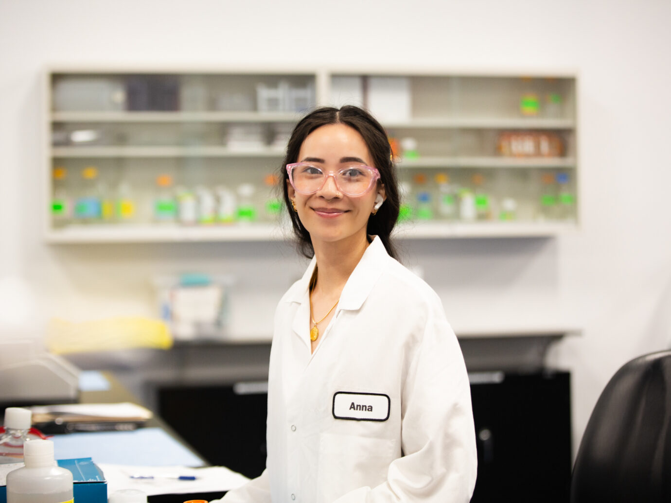 Smiling woman wearing pink glasses and a lab coat in a laboratory