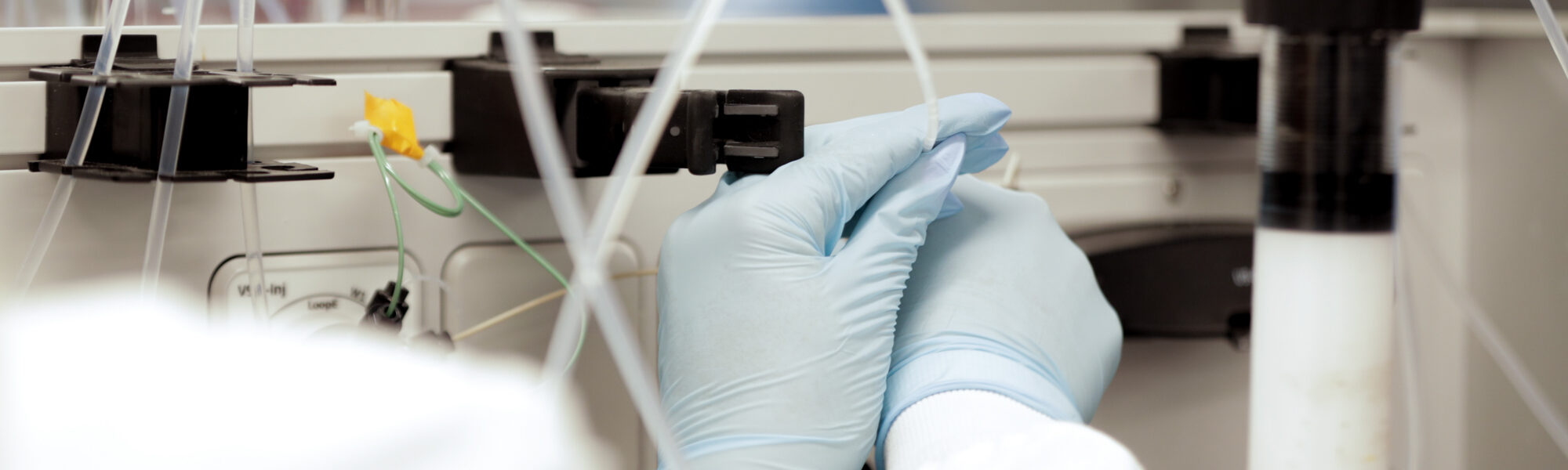 Gloved hand adjusting tubing on bioprocessing equipment in a lab