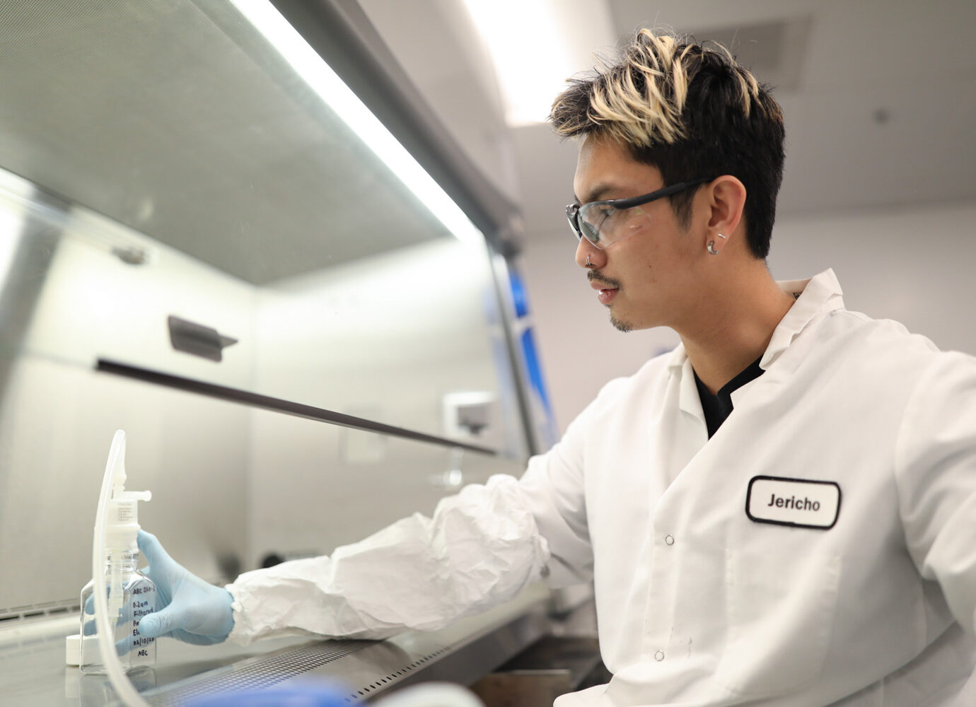 Man wearing glasses and a lab coat working near laboratory equipment