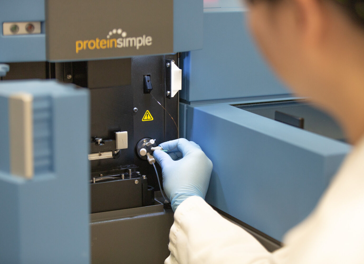 Gloved hand operating a ProteinSimple analytical instrument