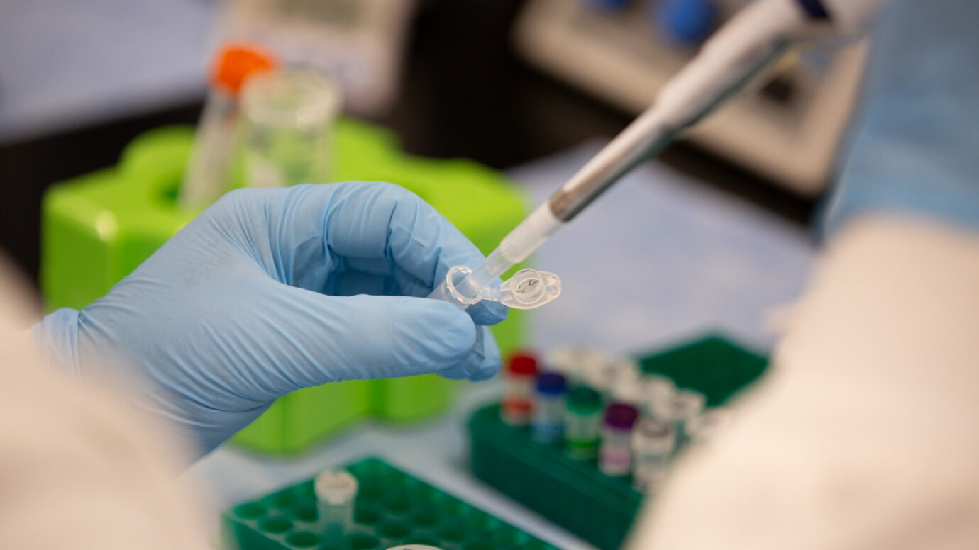 Close-up of a gloved hand using a pipette with a sample tube