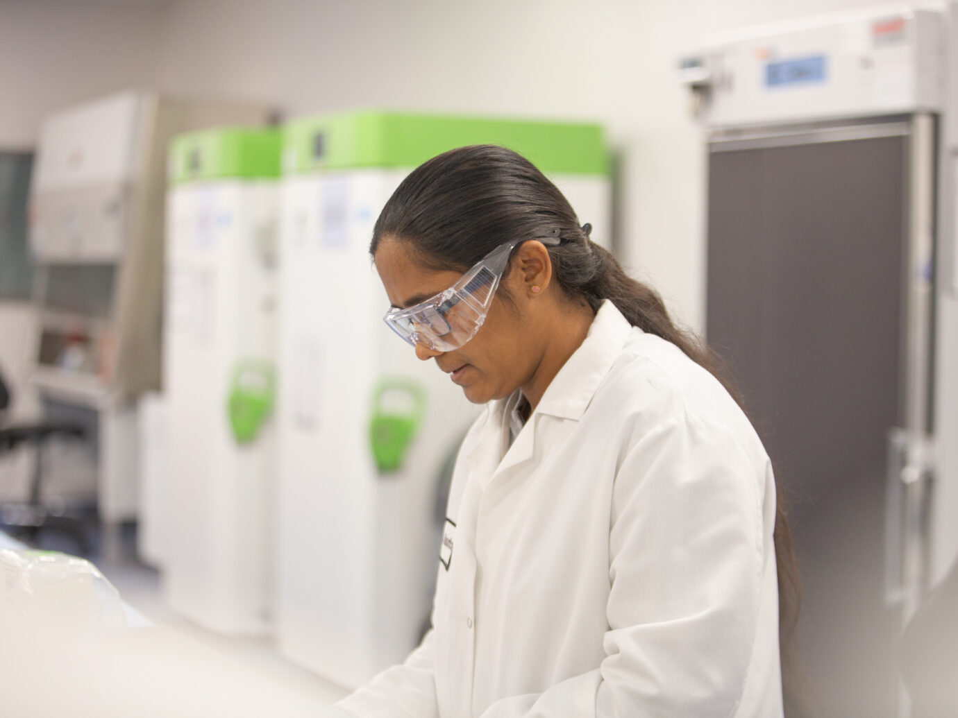 Female scientist wearing safety glasses and a lab coat in front of laboratory equipment