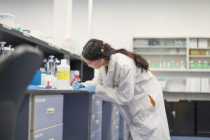 Female lab worker writing notes at a bench lined with lab supplies