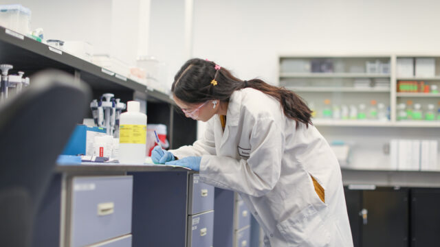 Female lab worker writing notes at a bench lined with lab supplies
