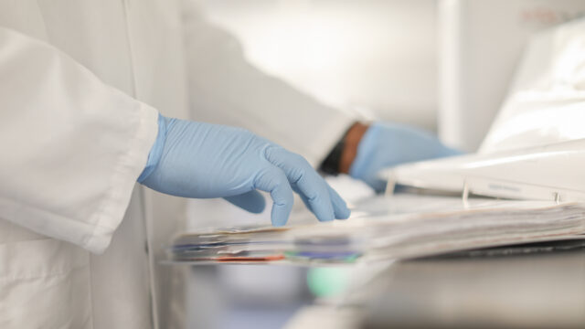 Gloved hand reaching for paperwork on a lab cart