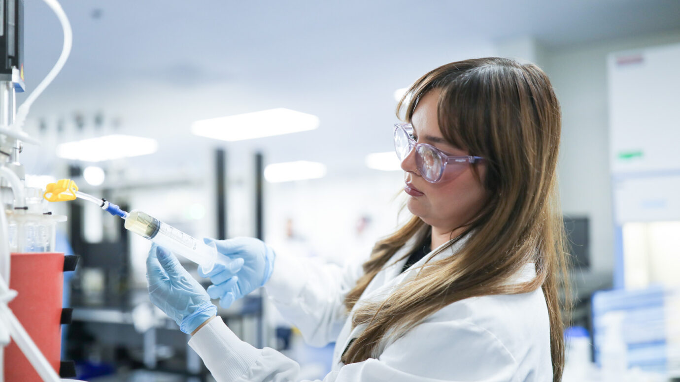 Woman wearing pink glasses using a pipette in a laboratory