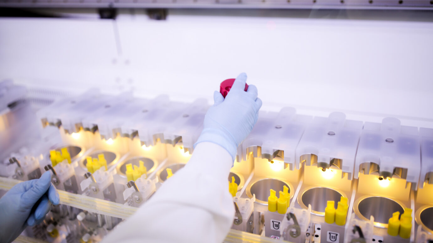 Gloved hand placing a red-capped vial into a laboratory equipment rack