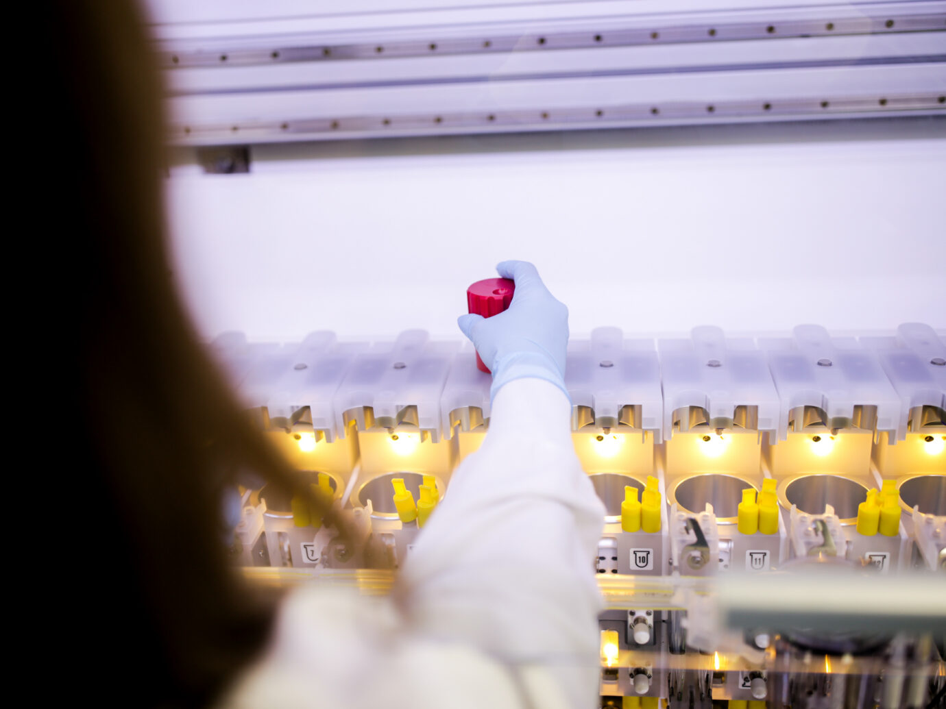 Gloved hand placing a red-capped vial into a laboratory equipment rack