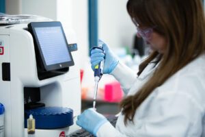 Female scientist using a pipette next to laboratory equipment with a digital display