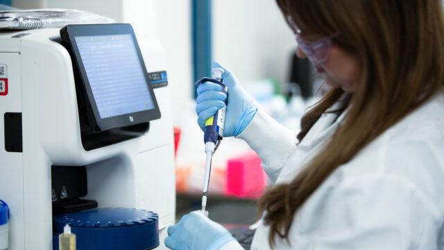 Female scientist using a pipette next to laboratory equipment with a digital display