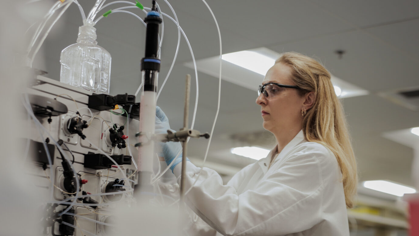Female scientist wearing safety glasses observing lab equipment with tubing