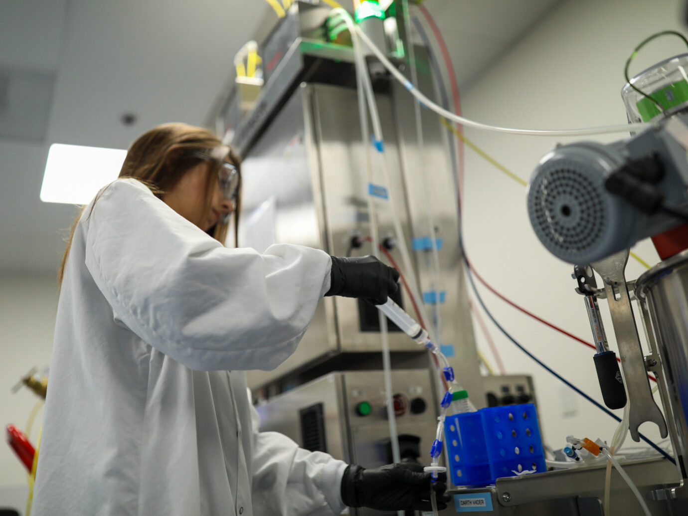 Scientist in a lab coat operating large bioprocessing equipment with tubing