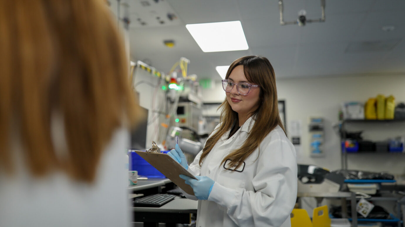 Two colleagues talking in a laboratory, one wearing glasses and a lab coat