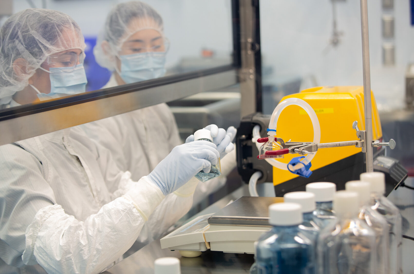 Two technicians in hairnets and masks working with manufacturing equipment in a cleanroom