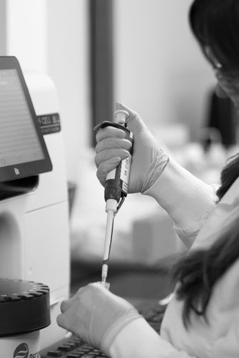 Gloved hand holding a pipette near laboratory equipment