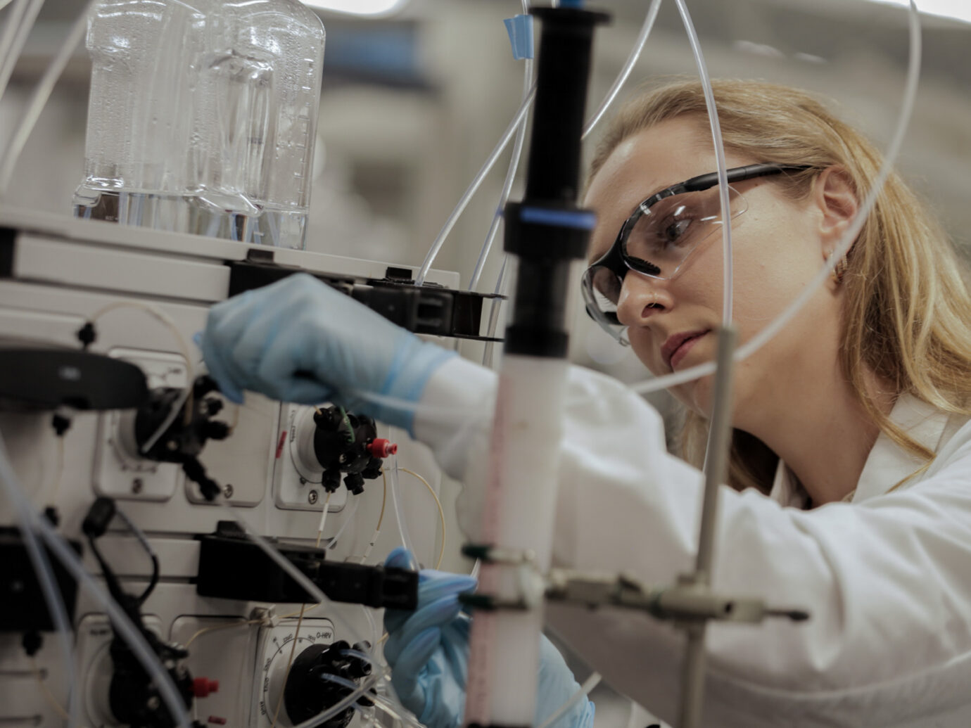Female scientist wearing safety glasses examining bioprocessing equipment with tubing