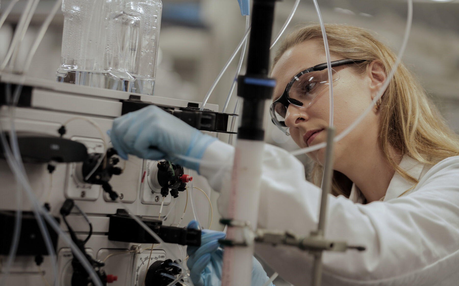 Female scientist wearing safety glasses examining bioprocessing equipment with tubing